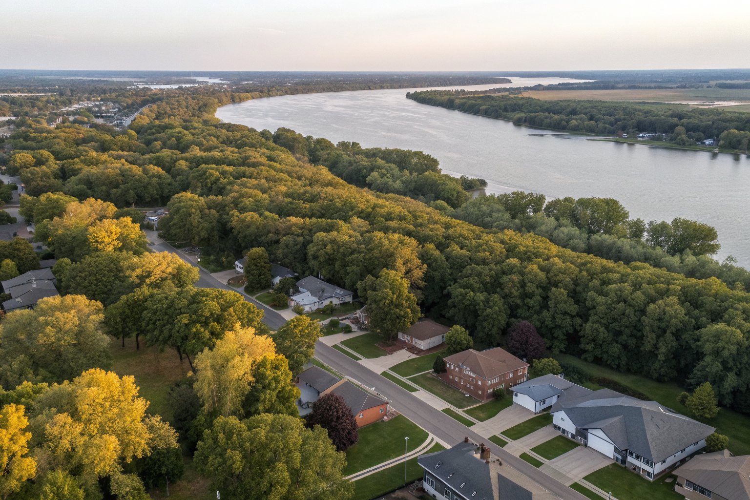 Aerial view of a tree-lined suburb with shingle roofs along a wide river in late summer